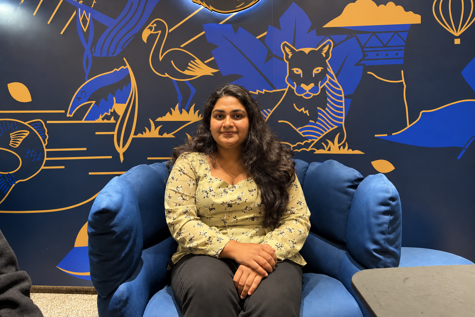 About Mansi Jamdade, UX/UI designer, seated in a blue armchair